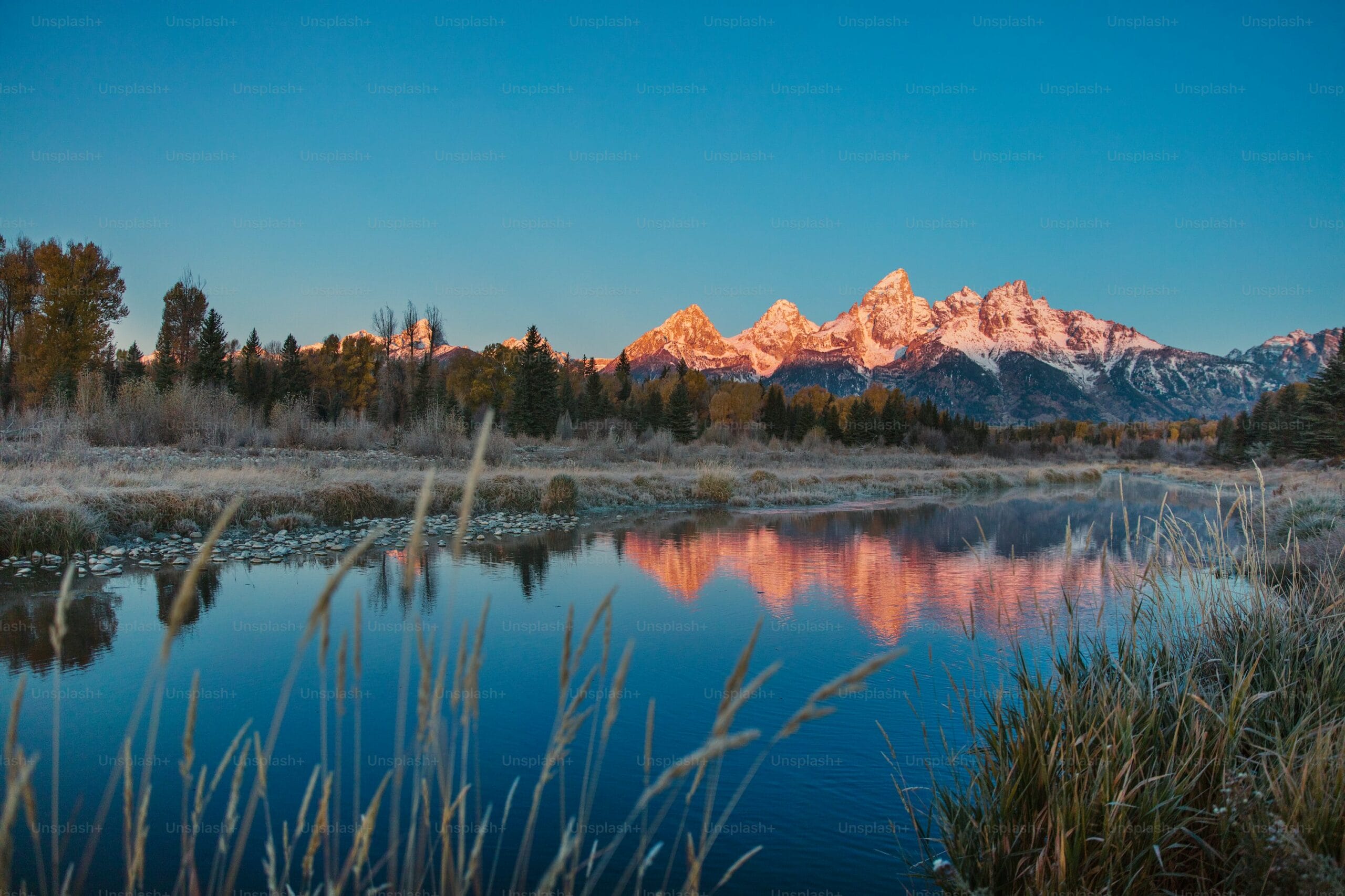 Sunset over snow-covered mountain range and lake reflection.