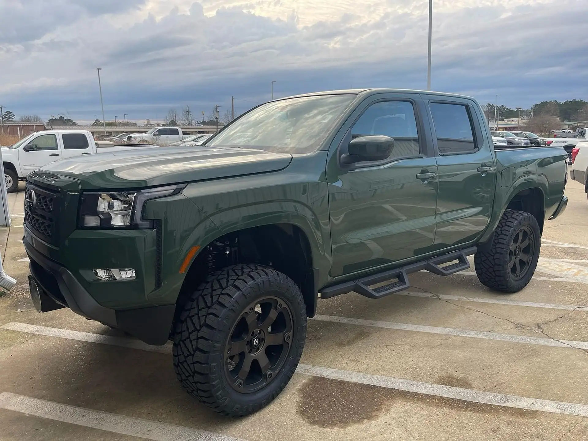 Green pickup truck parked in lot under cloudy sky. Nissan Frontier wheels